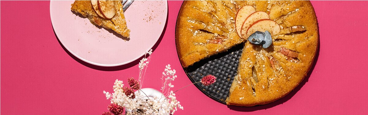 Apfelkuchen in einer Springform und daneben ein Teller mit einem Kuchenstück