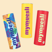 Drei mymuesli -Dosen in Blau, Gelb und Pink sind dynamisch versetzt auf einem hellgelben Hintergrund angeordnet.