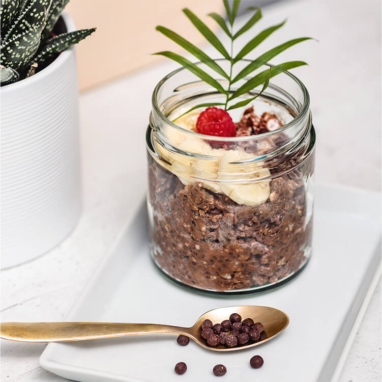 Banane Schoko Overnight Oats in einem Glas mit Bananenscheiben und einem Löffel daneben