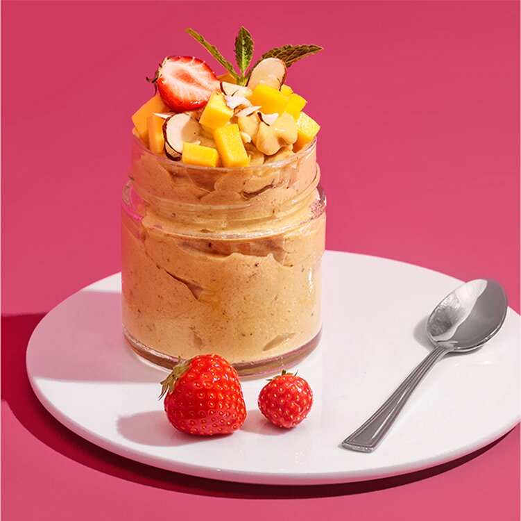 Mango Nicecream in einem Glas mit Mango, Erdbeeren und Nüssen dekoriert