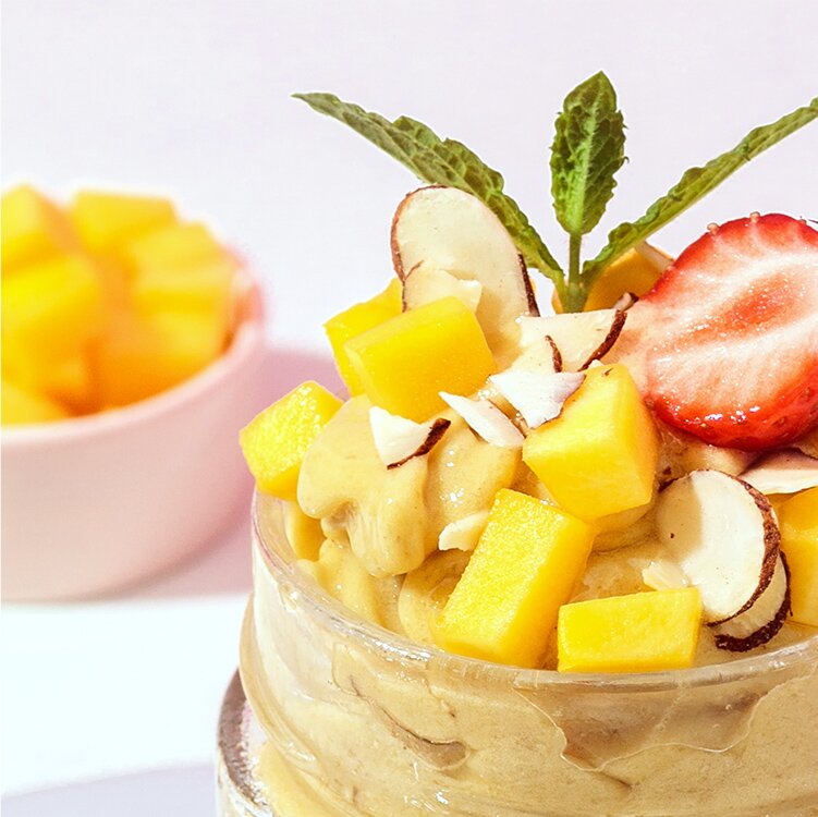 Mango Nicecream in einem Glas mit Mango, Erdbeeren und Nüssen dekoriert