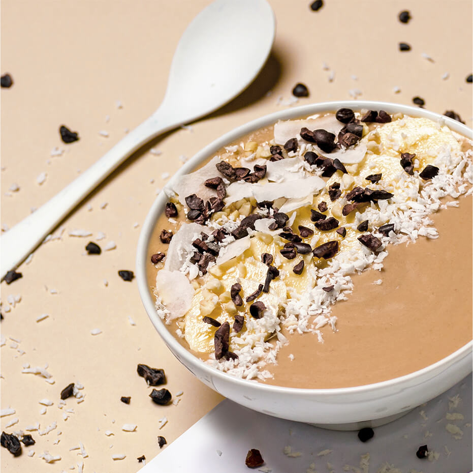 Nicecream mit Erdnussbutter mit Bananenscheiben und Kokosraspeln dekoriert