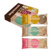 Eine Packung "Nut Butter Balls" neben drei einzeln verpackten Riegeln in den Sorten Peanut, Almond und Strawberry auf schwarzem Hintergrund.