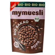 Eine Packung "mymuesli Bio Kakao Pops" in einer braun-rosa Tüte auf grünem Hintergrund, mit einer Abbildung der schokolierten Getreide-Pops.