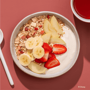 Disney Guten Morgen Löwe Müsli in einer Müslischale mit Bananenscheiben, Erdbeeren, Apfelspalten und Joghurt.