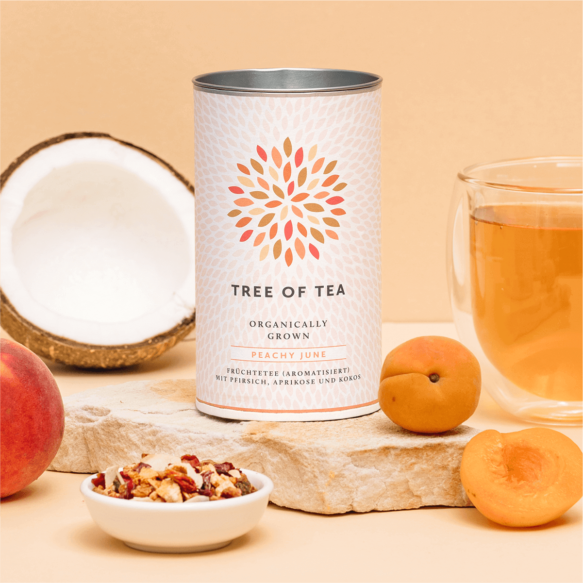 Tree of Tea Bio Peachy June neben einem Glas Tee, Pfirsichen und einer halben Kokosnuss