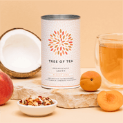 Tree of Tea Bio Peachy June neben einem Glas Tee, Pfirsichen und einer halben Kokosnuss