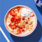 Eine rosafarbene Schüssel mit Müsli, Joghurt und frischen Erdbeerstücken, von oben fotografiert auf einem kräftigen blauen Hintergrund.