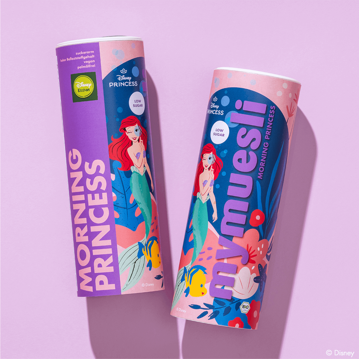 Zwei mymuesli -Dosen der "Morning Princess" Edition mit Arielle-Motiv, nebeneinander liegend auf einem hellvioletten Untergrund.