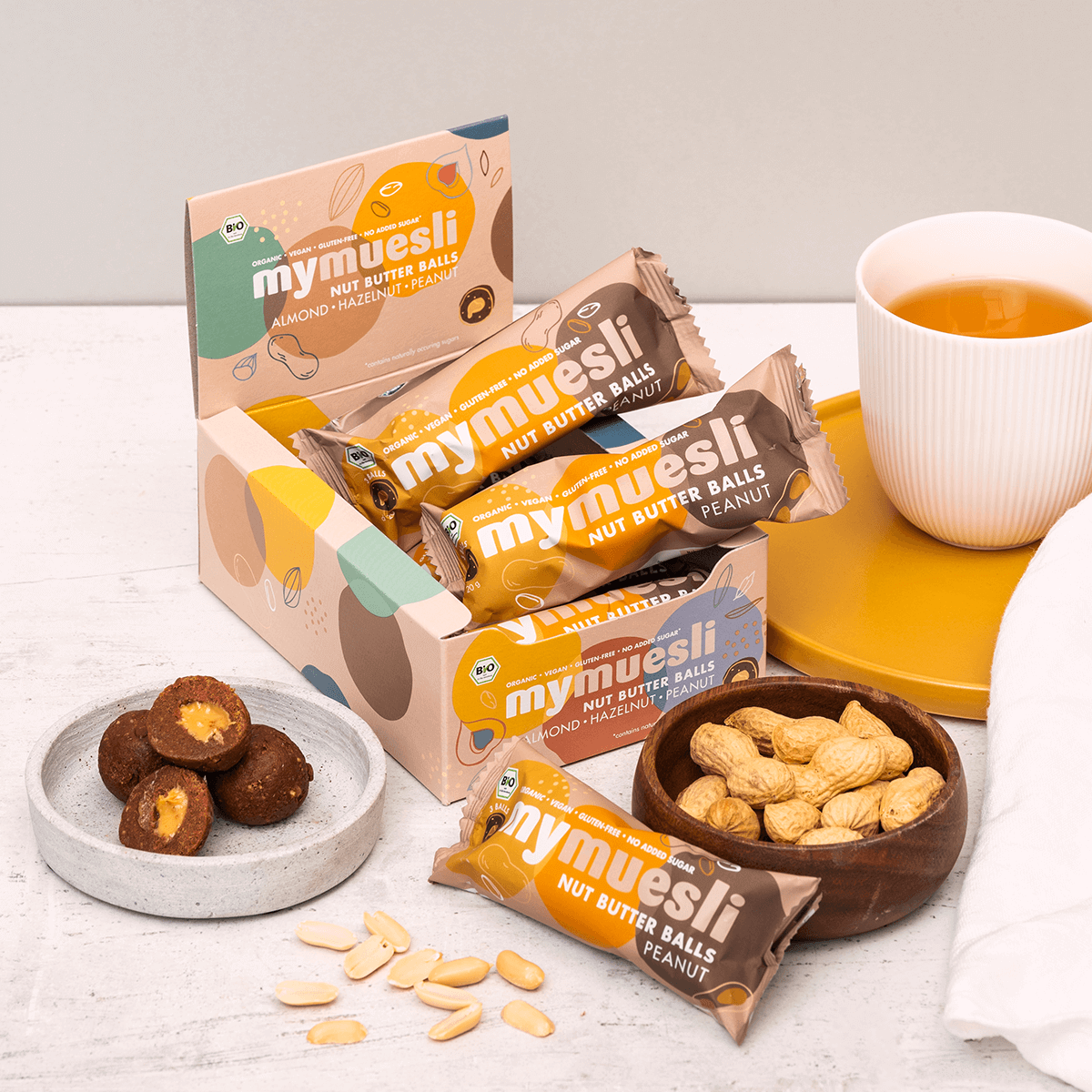 Lifestyle-Aufnahme der Erdnuss-Nut-Butter-Balls neben frischen Erdnüssen auf einer Arbeitsfläche.