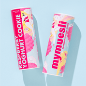 Zwei mymuesli -Dosen der Sorte "Raspberry Yoghurt Cookie" mit pastellfarbenem Design, nebeneinander liegend auf einem hellblauen Hintergrund.
