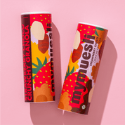 Zwei mymuesli -Dosen mit Erdbeer-Design liegen nebeneinander auf einem hellrosa Hintergrund.