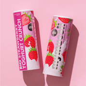 Zwei mymuesli -Dosen der Sorte "Strawberry Yoghurt Crunch" mit Erdbeer-Motiven, nebeneinander liegend auf einem hellrosa Hintergrund.