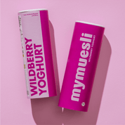 Zwei mymuesli -Dosen der Sorte "Wildberry Yoghurt" – eine hellrosa und eine dunkelpink – liegen nebeneinander auf einem fliederfarbenen Hintergrund.