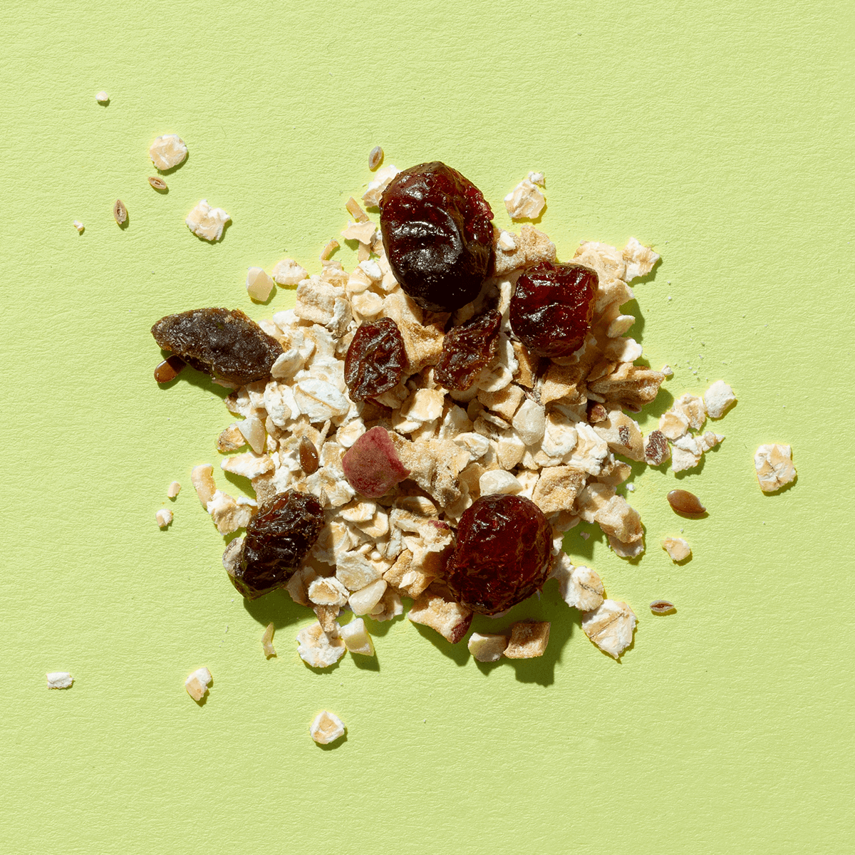 Eine Nahaufnahme der Bircher Müsli-Mischung auf hellgrünem Grund mit Haferflocken, Rosinen und getrockneten Apfelstücken.