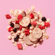 Eine lose Mischung aus Müsli-Zutaten auf rosa Grund: Haferflocken, getrocknete Erdbeerstücke, Bananenscheiben und dunkle Beeren.