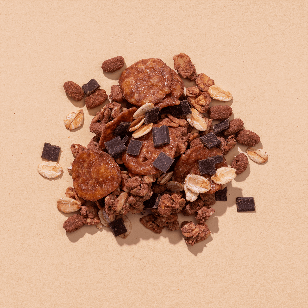Nahaufnahme einer Müsli-Mischung mit Schoko-Crunchies, dunklen Schokoladenstücken und getrockneten Bananenscheiben auf beigem Grund.