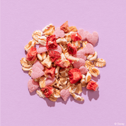 Eine bunte Müsli-Mischung auf violettem Hintergrund, die kleine rosa Schoko-Herzen und getrocknete Erdbeerstücke enthält.