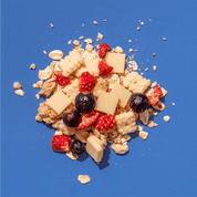 Nahaufnahme einer Müslimischung auf blauem Grund mit weißen Schokoladenstücken, Bananenchips und gefriergetrockneten Erdbeeren.