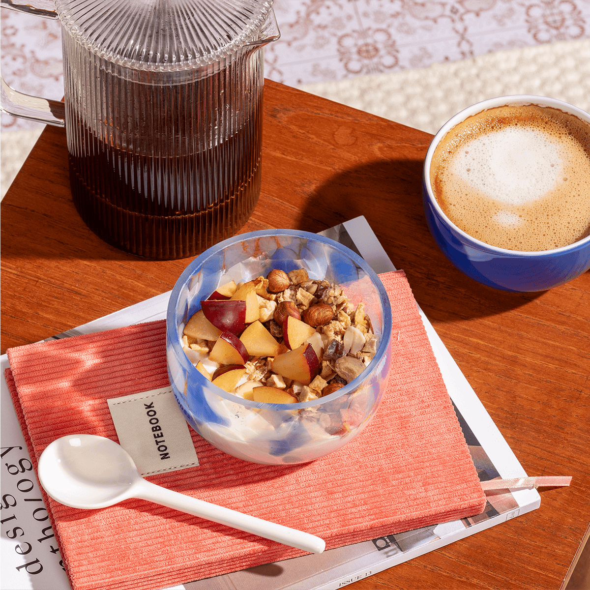 Gemütliche Frühstücksszene im Freien mit einer Müsli-Schüssel, einer French Press und einer Tasse Kaffee auf einem Holztisch.