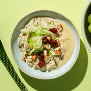 Eine helle Schüssel mit Bircher Müsli, garniert mit geraspeltem grünem Apfel und Nüssen auf einem hellgrünen Hintergrund.
