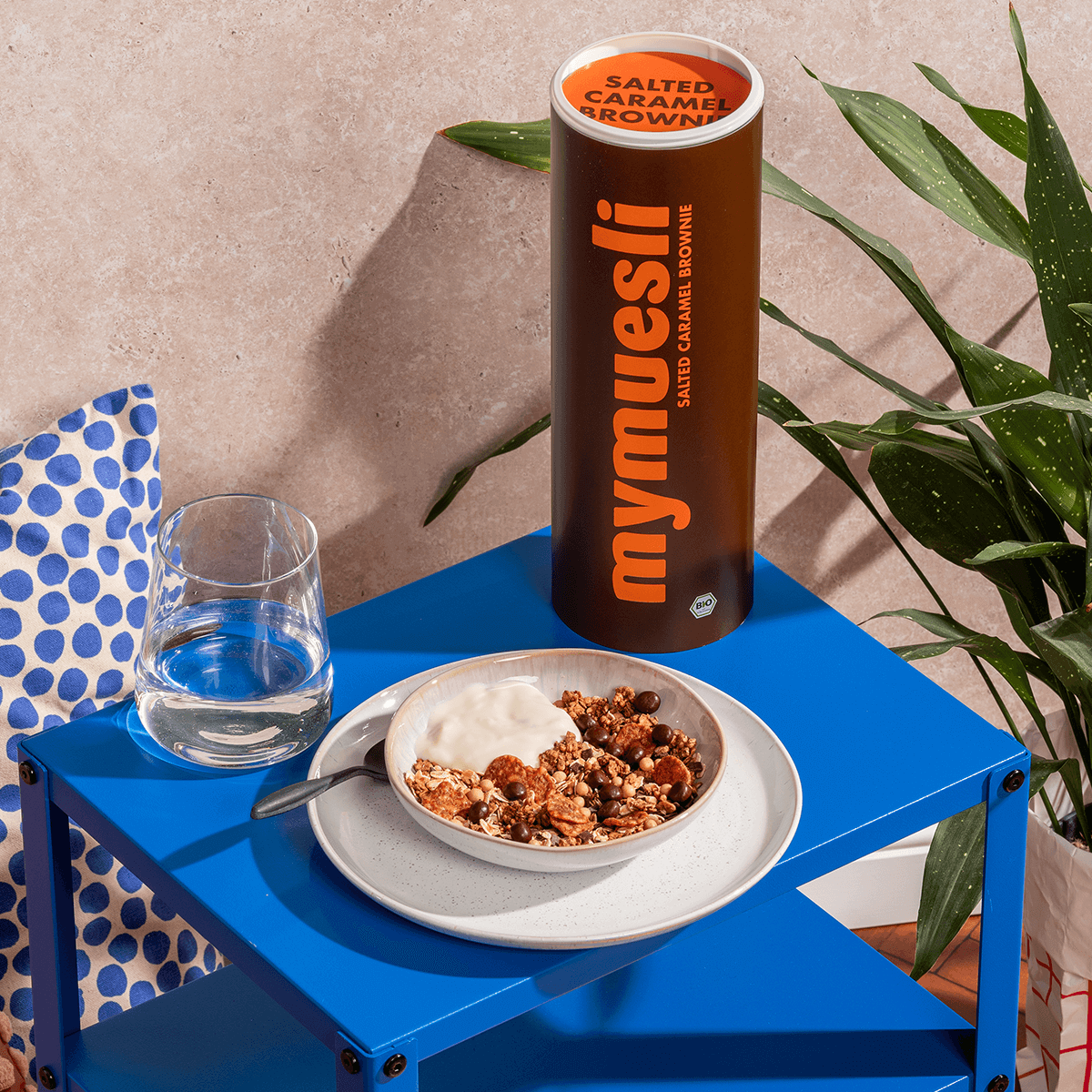 Salted Caramel Brownie in einer Frühstücksszene auf einem kleinen blauen Tisch mit einer Schüssel und einem Glas. Vermutlich draußen.