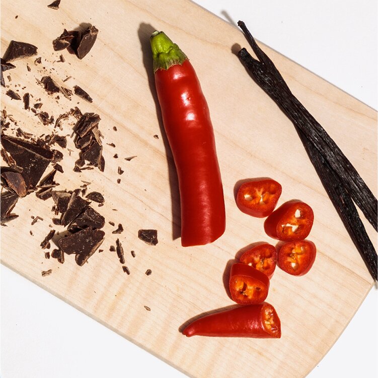 Chili, Vanilleschoten und Schokolade auf einem Holzbrett