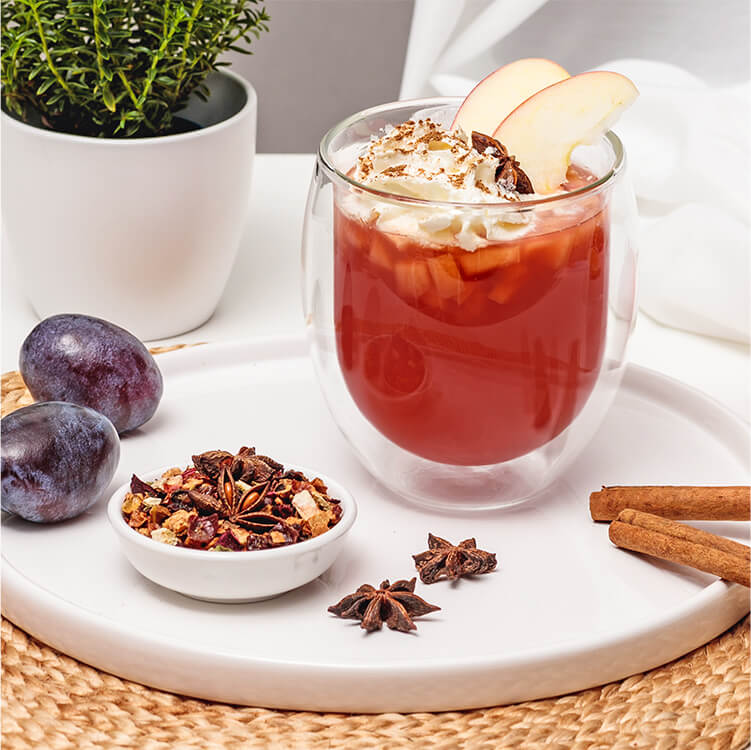 Bratapfel Punsch mit Zimtsahne, mit einem Apfel, Pflaumen, Tee und Gewürzen daneben